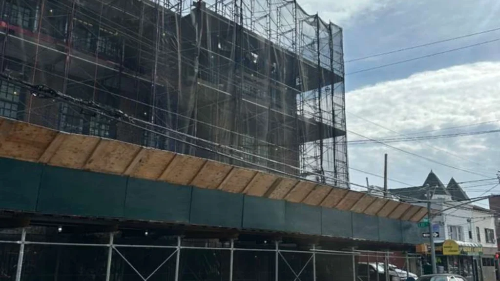 Full building pipe scaffolding with debris netting and sidewalk shed installed on urban construction site in Brooklyn NY